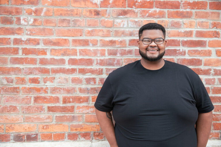 Cheston Downs, KARMA jack employee, smiling for the camera against red brick