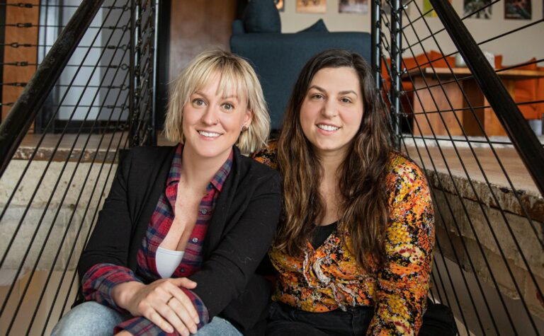 a blonde-haired woman and a brunette-haired woman sitting side by side for the camera