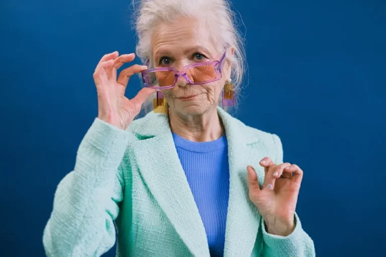older woman posing for picture and holding onto her purple glasses on her face